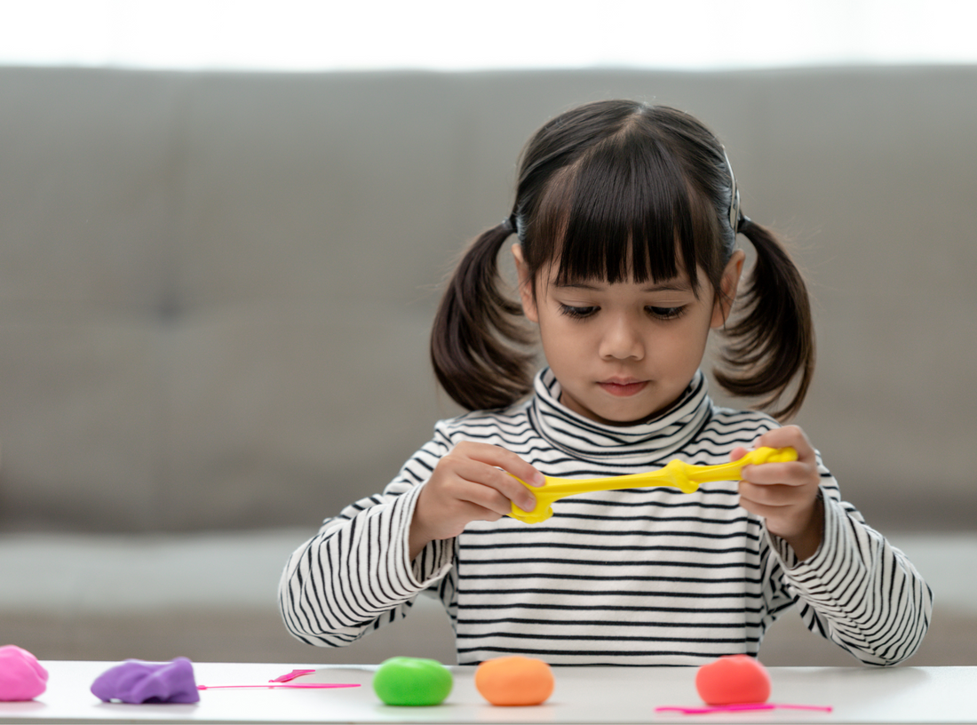 Young girl developing fine motor skills while playing with scented sensory playdough at home.